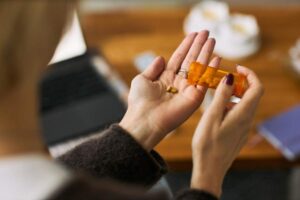 A family member helps an older adult use a pill organizer at a kitchen table, with medication bottles nearby.