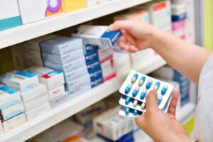 A pharmacist showing a patient two different-looking prescription bottles and explaining the pills at a pharmacy counter.