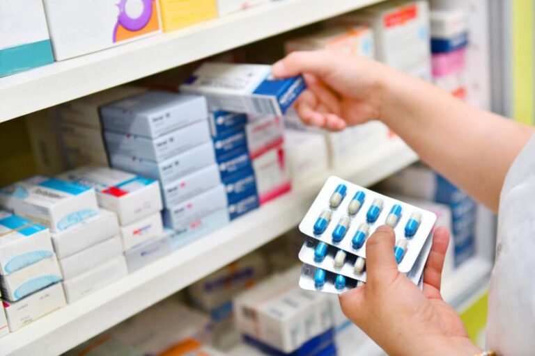 A pharmacist showing a patient two different-looking prescription bottles and explaining the pills at a pharmacy counter.