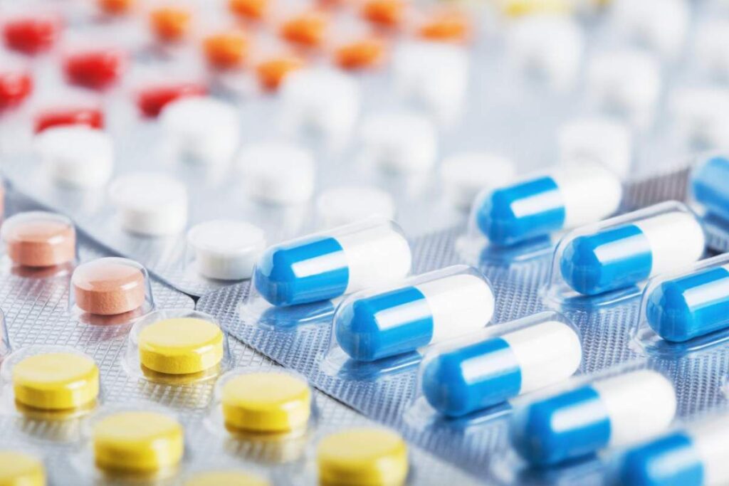 A person reviewing a medication guide at a kitchen table with a glass of water and pill bottle nearby.