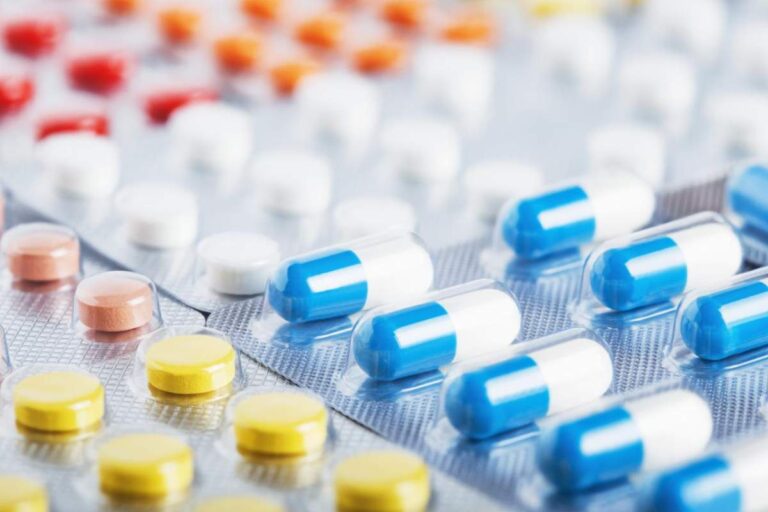 A person reviewing a medication guide at a kitchen table with a glass of water and pill bottle nearby.